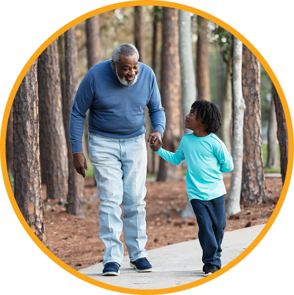 A grandfather and his grandson walking together and holding hands on a wooded path