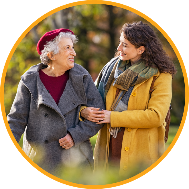 An older woman and a younger woman walking arm in arm together on an autumn path
